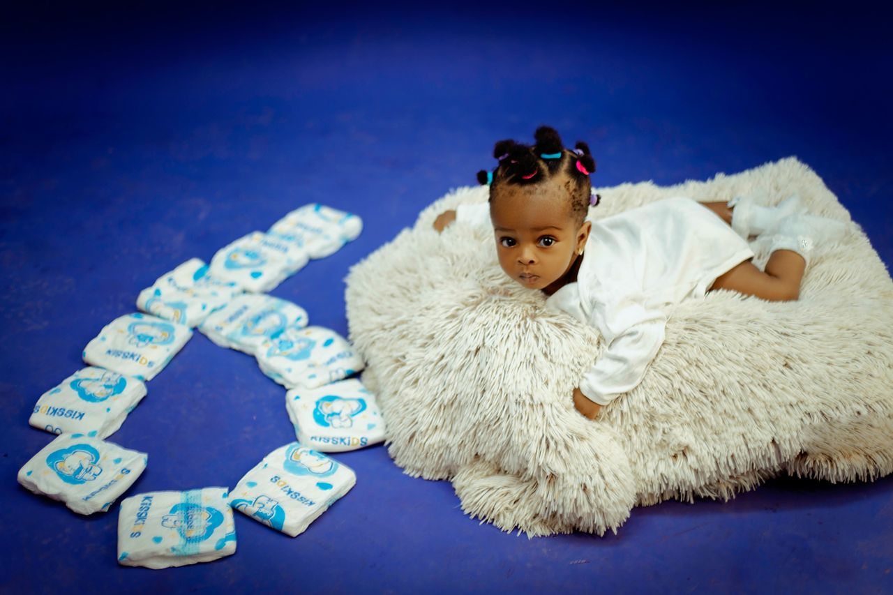 Cute baby lying on a soft rug with diapers arranged in a heart shape.